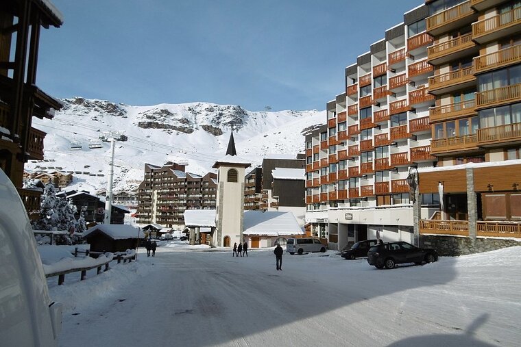 A snowy street with a few cars parked in front of a building