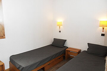 A bedroom with two beds and two lamps on the wall