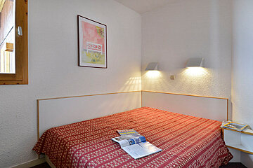 A bed with a red blanket and a magazine on it