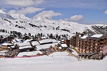 A snowy landscape with buildings and mountains in the background