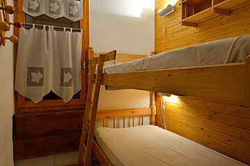 A bunk bed with a ladder and a window with curtains with leaves on them