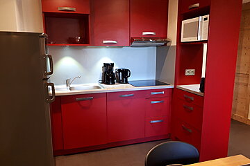 A small kitchen with red cabinets and a microwave