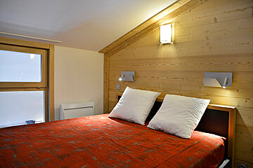 A bed with a red blanket and white pillows in a bedroom