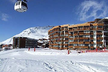 A ski lift is going up a snowy slope in front of a building that says l' ermitage