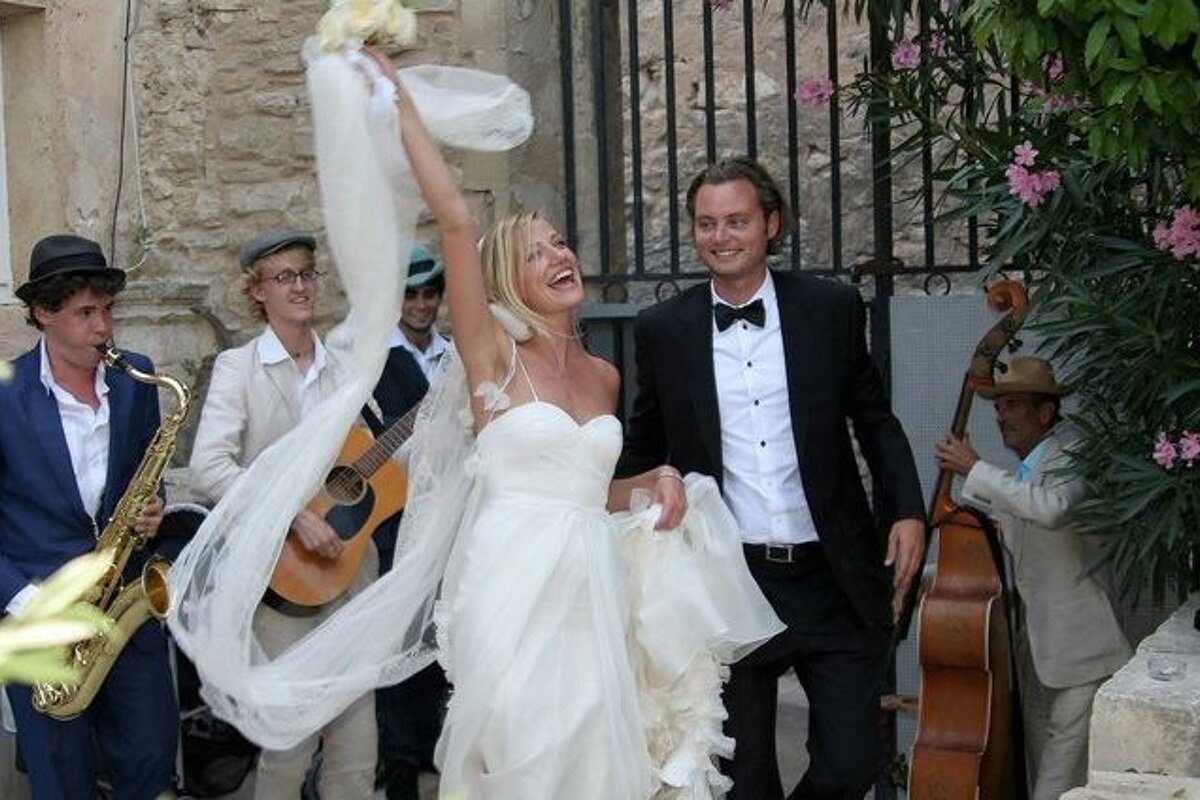 A man playing a saxophone stands behind a bride and groom