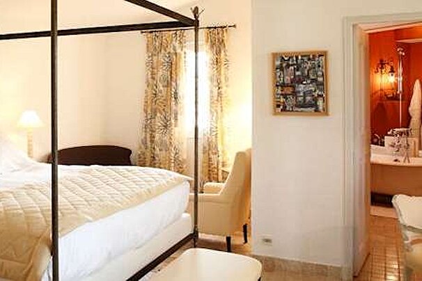 Metal four poster bed with white sheets and red bathroom to the side