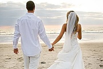 A bride and groom are walking on the beach holding hands