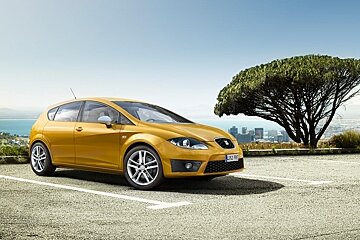 A yellow car is parked in a parking lot with a tree in the background
