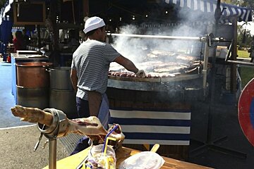 A man in a striped shirt is cooking meat on a grill