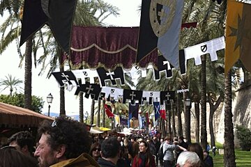 A crowd of people are walking down a street with flags and banners hanging from the trees