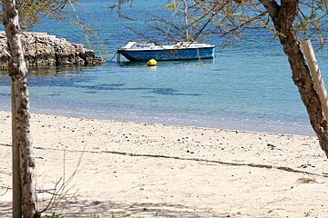 photo of a white sand beach with sea and a boat in the background