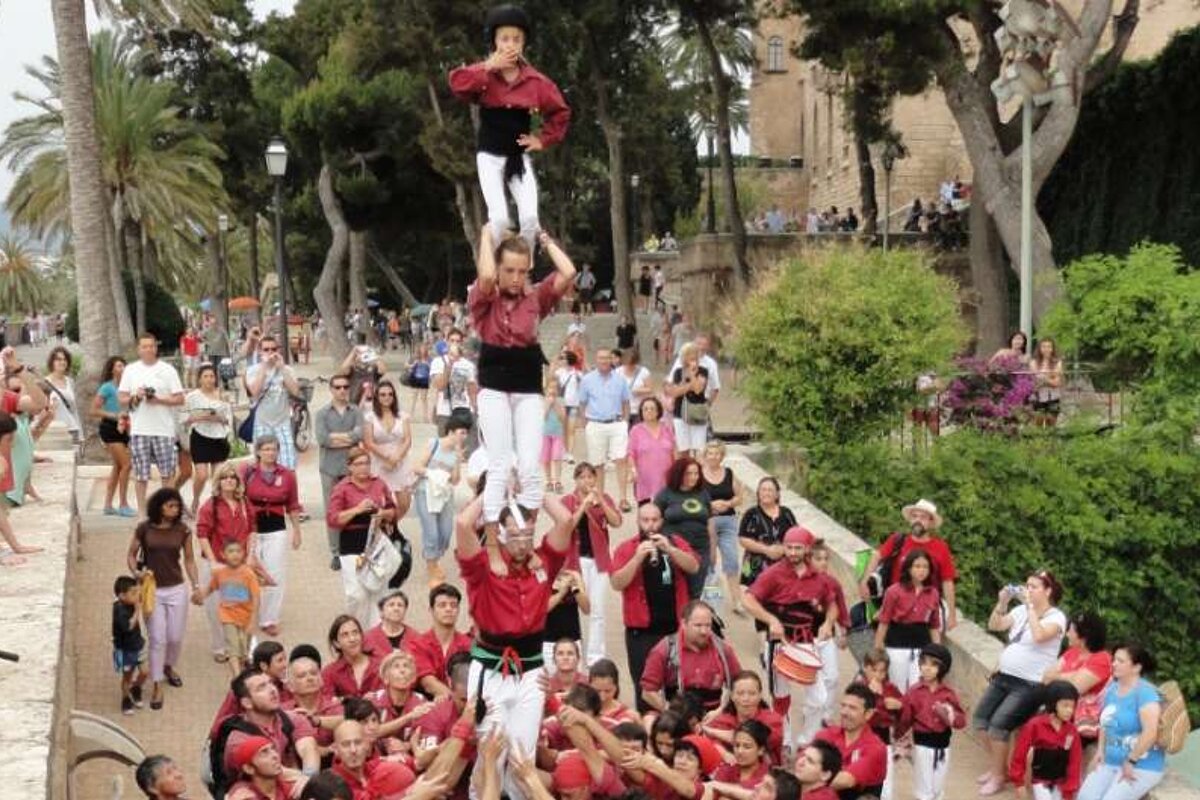 A crowd of people are gathered in a park with a man holding a child on his shoulders