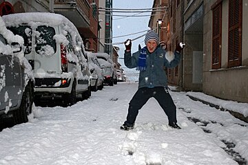 Child in snowy street with snowballs in hand