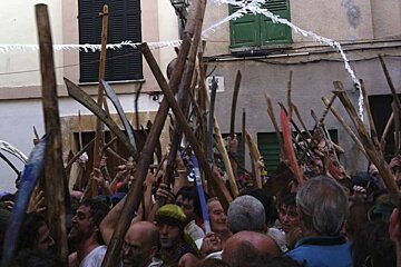 A crowd of people holding sticks in front of a building with a sign that says ' a ' on it