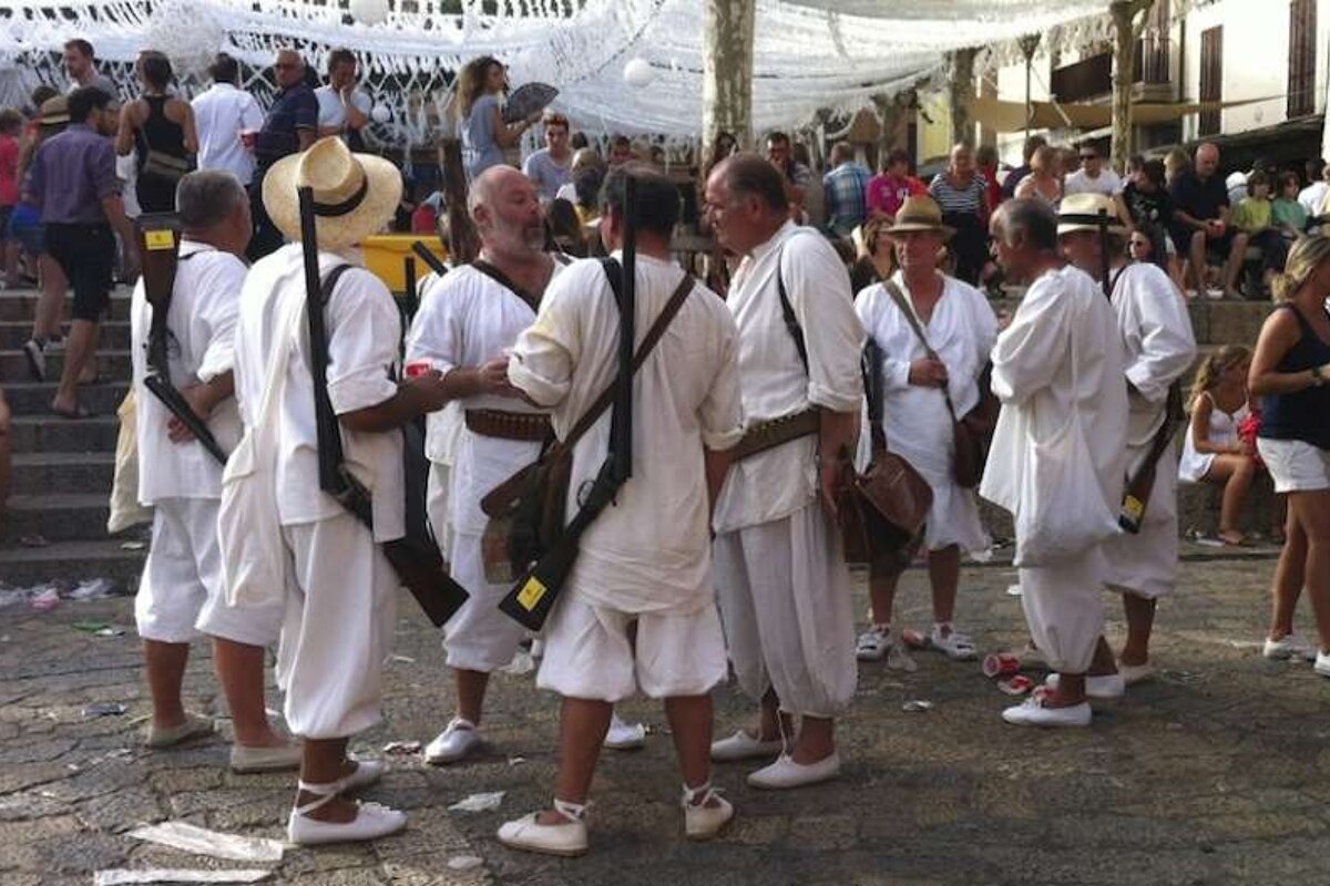 A group of men wearing white shirts and hats are standing in a crowd