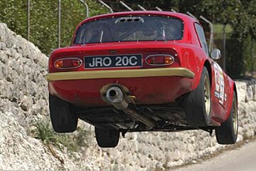 Red rally car taking off over bump in road