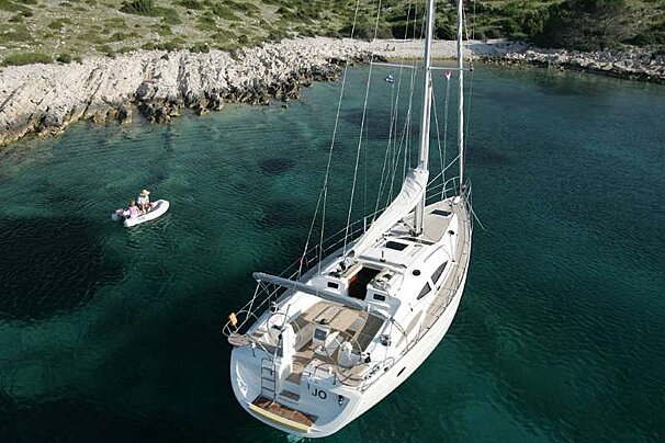 an image of a large white sailing yacht moored in clear waters by a rocky coast with its tender nearby