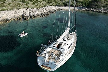 an image of a large white sailing yacht moored in clear waters by a rocky coast with its tender nearby