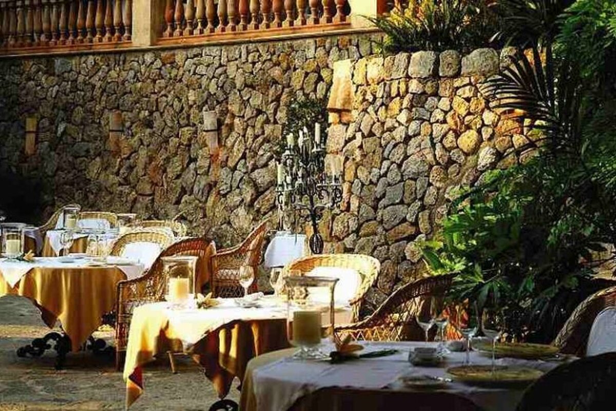 an image of a row of tables next to a stone wall in dappled light