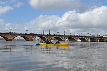 People in yellow kayaks on a river with a bridge in the background