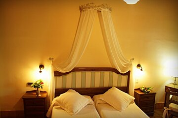 A warm, inviting bedroom featuring twin beds with a delicate canopy, bedside tables, and sconce lighting for a cozy ambiance.