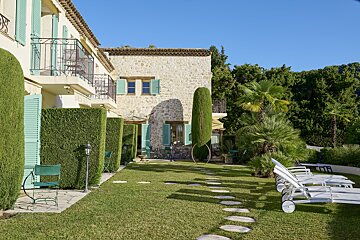 A stone building with blue shutters sits next to a lush green lawn