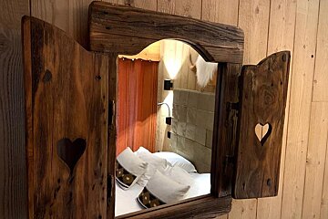 A bed is reflected in a wooden mirror with heart shaped shutters