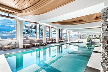 A large indoor swimming pool with chairs and a ski lift in the background