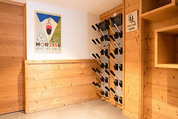 A cozy ski room with wooden paneling, a vintage Morzine poster, and a wall-mounted ski boot drying rack with an 
