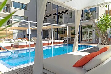 A sunny resort with a sparkling blue pool, white canopy daybeds, and modern hotel buildings, promising relaxation.