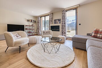 A cozy, modern living room with large windows showcasing stunning mountain views. It features a fireplace, plush seating, and a stylish coffee table.