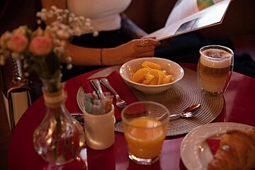A woman sits at a table with a bowl of fruit and a glass of orange juice