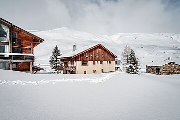 A snowy landscape with a house in the foreground and mountains in the background