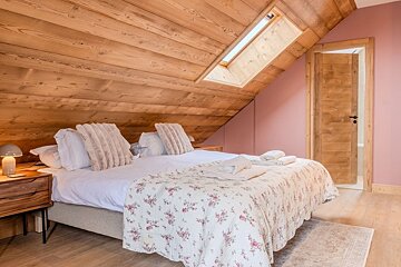 Cozy attic bedroom with a slanted wooden ceiling, a skylight, and a bed with a floral quilt against pink walls.
