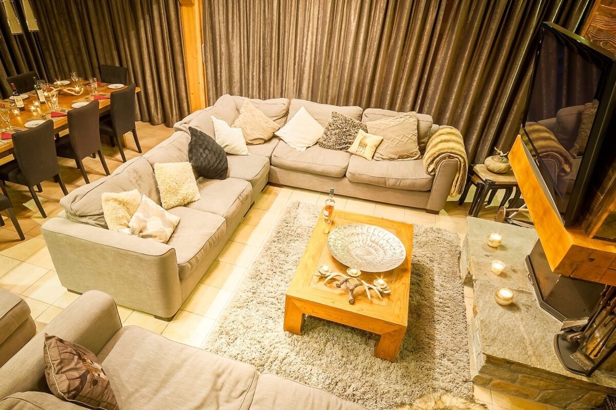 A cozy, spacious living room with a large sectional sofa, rustic coffee table, and fireplace. A dining table is visible, creating a warm, inviting atmosphere.