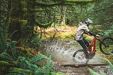 A person riding a bike through a stream in the woods