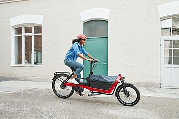 A woman wearing a red helmet is riding a red cargo bike