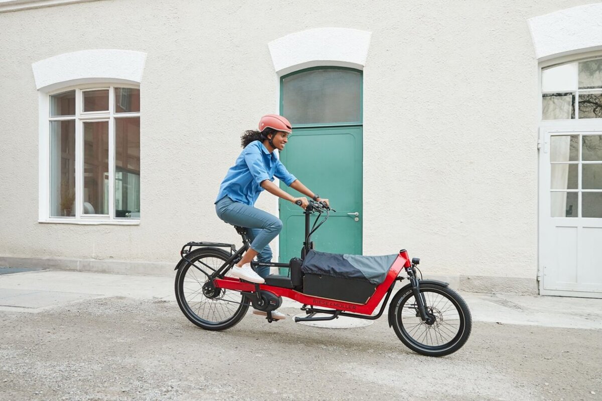 A woman wearing a red helmet is riding a red cargo bike