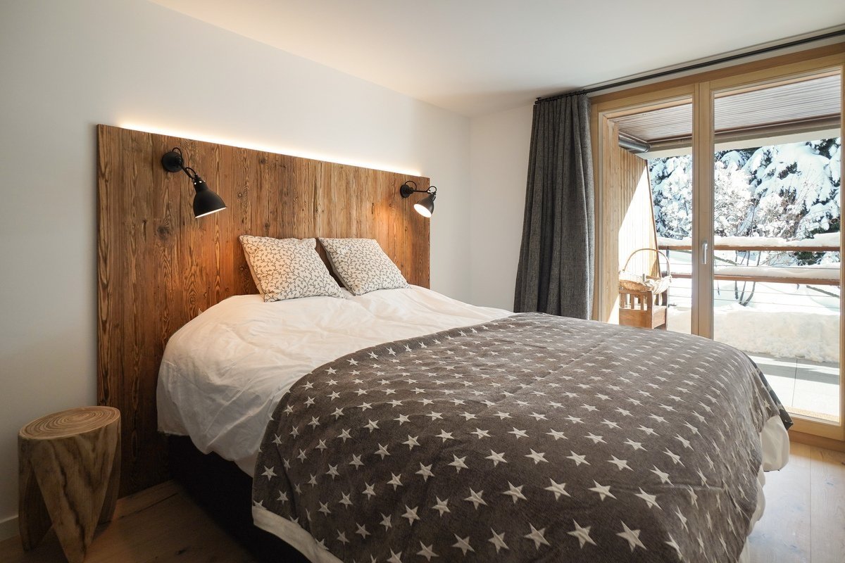 Cozy bedroom with rustic wooden headboard, star blanket, and a large window overlooking a snowy landscape.