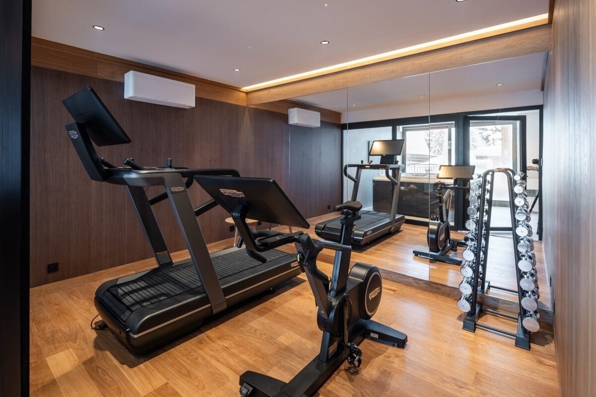 Sleek home gym with two treadmills, an exercise bike, dumbbell rack, and a large mirror reflecting the space, set against warm wooden walls.