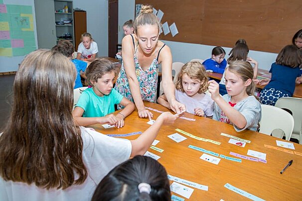 A group of children are sitting around a table and one girl is wearing a shirt that says