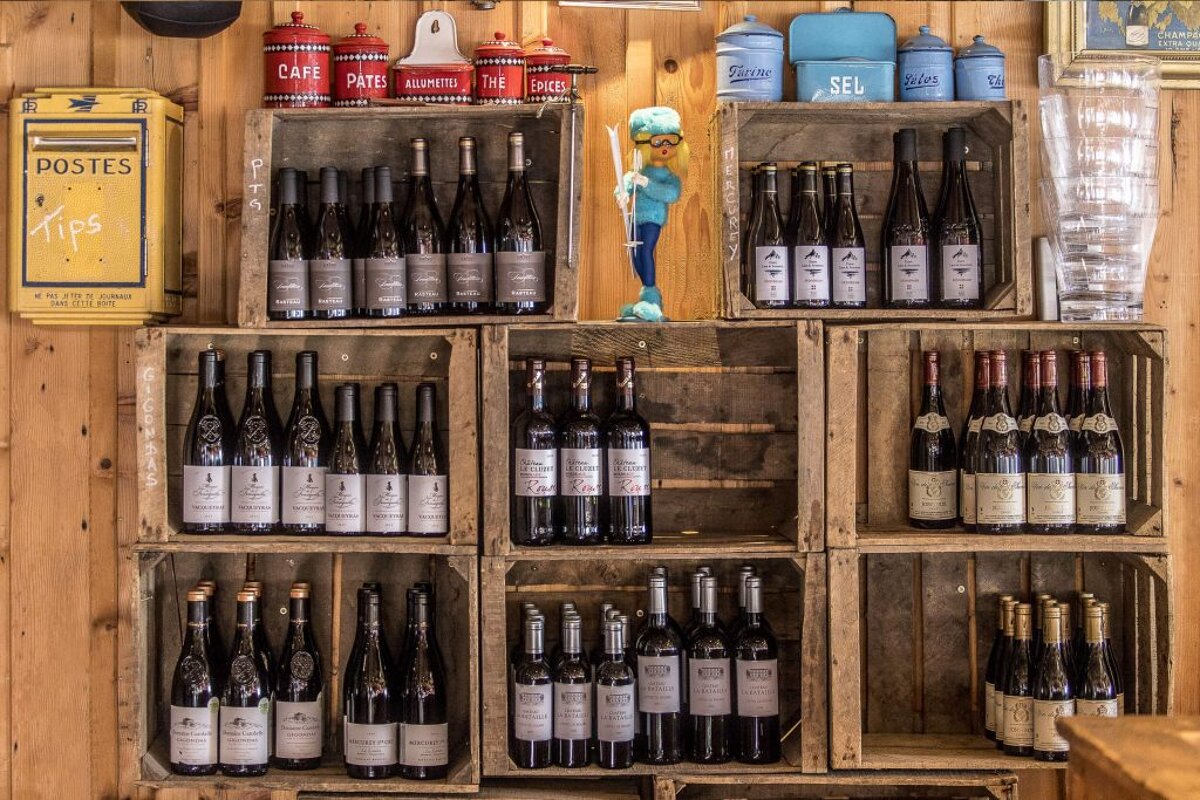 Bottles of wine are displayed in wooden crates in front of a post box that says postes