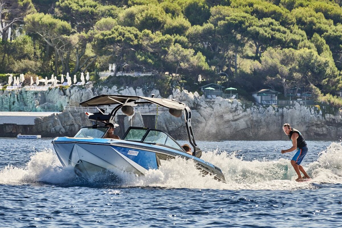 A man is riding a wave on the back of a boat that says ' jet ski ' on the side