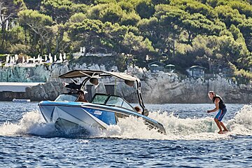 A man is riding a wave on the back of a boat that says ' jet ski ' on the side