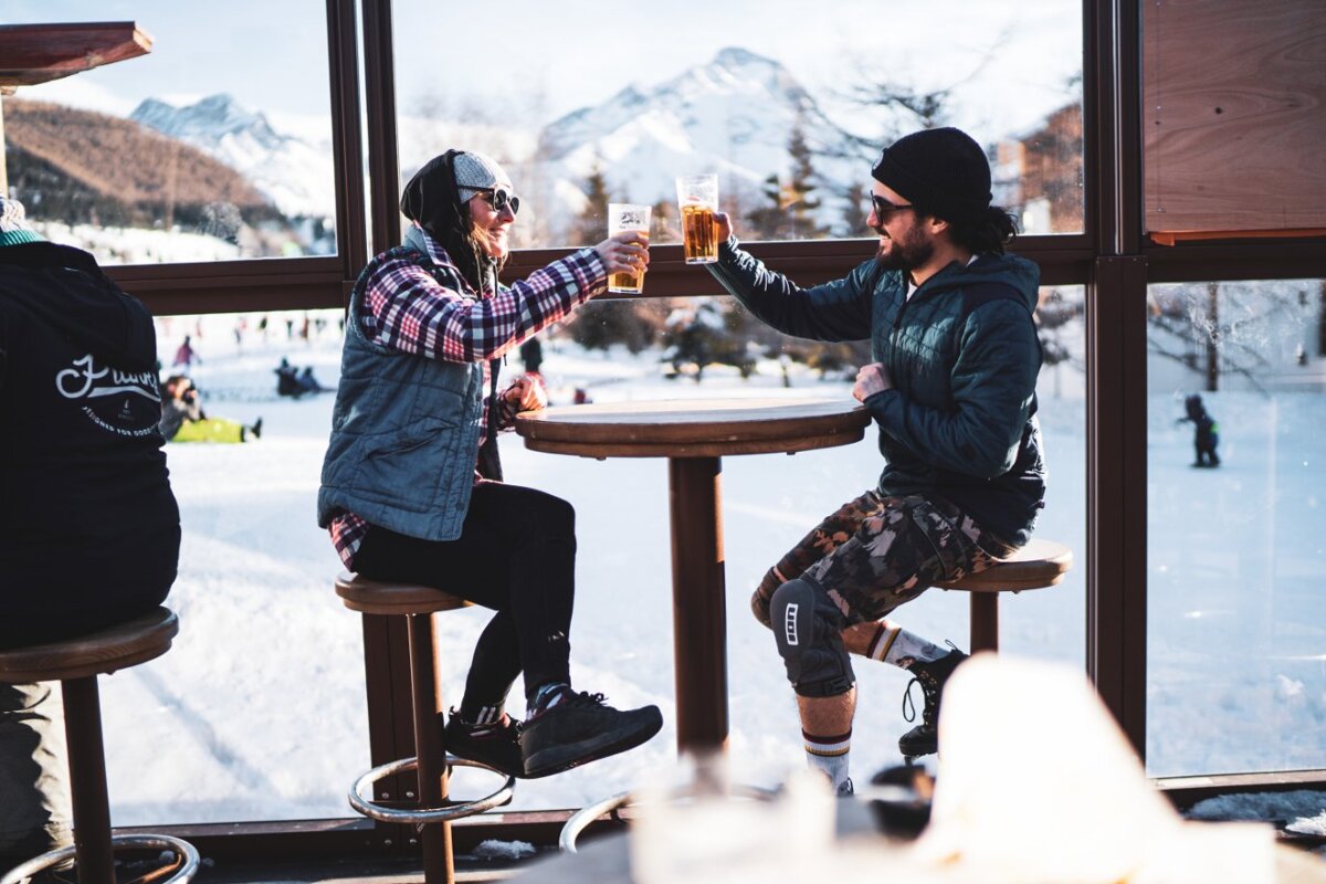 A man and a woman are sitting at a table toasting with beer