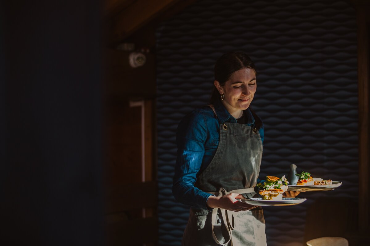 A woman in an apron is carrying two plates of food