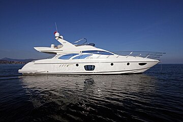 A large white yacht is moored on tranquil blue water beneath a clear sky, reflecting in the water with distant land visible.