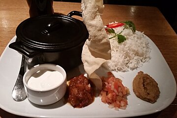 a white plate with a black pot & sauces on the side