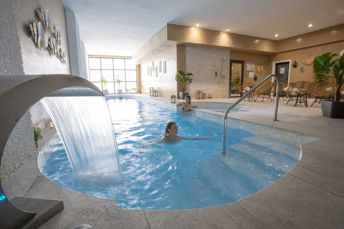 Two people are swimming in a pool with a waterfall