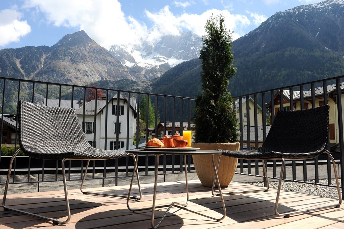 A bottle of champagne sits on a balcony with mountains in the background